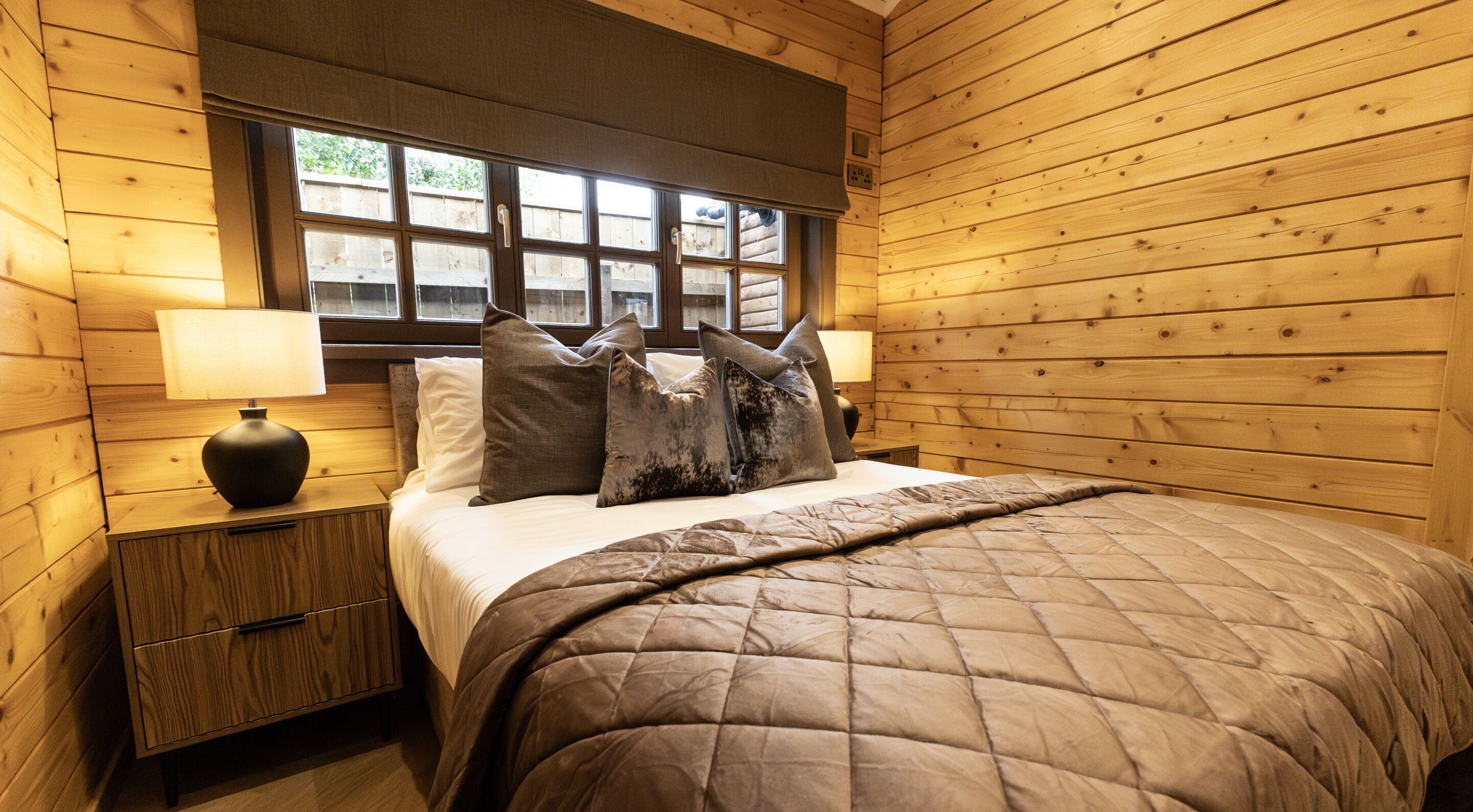 Un dormitorio tipo cabaña de madera con una cama, dos mesitas de noche, un ventanal y vistas al exterior.