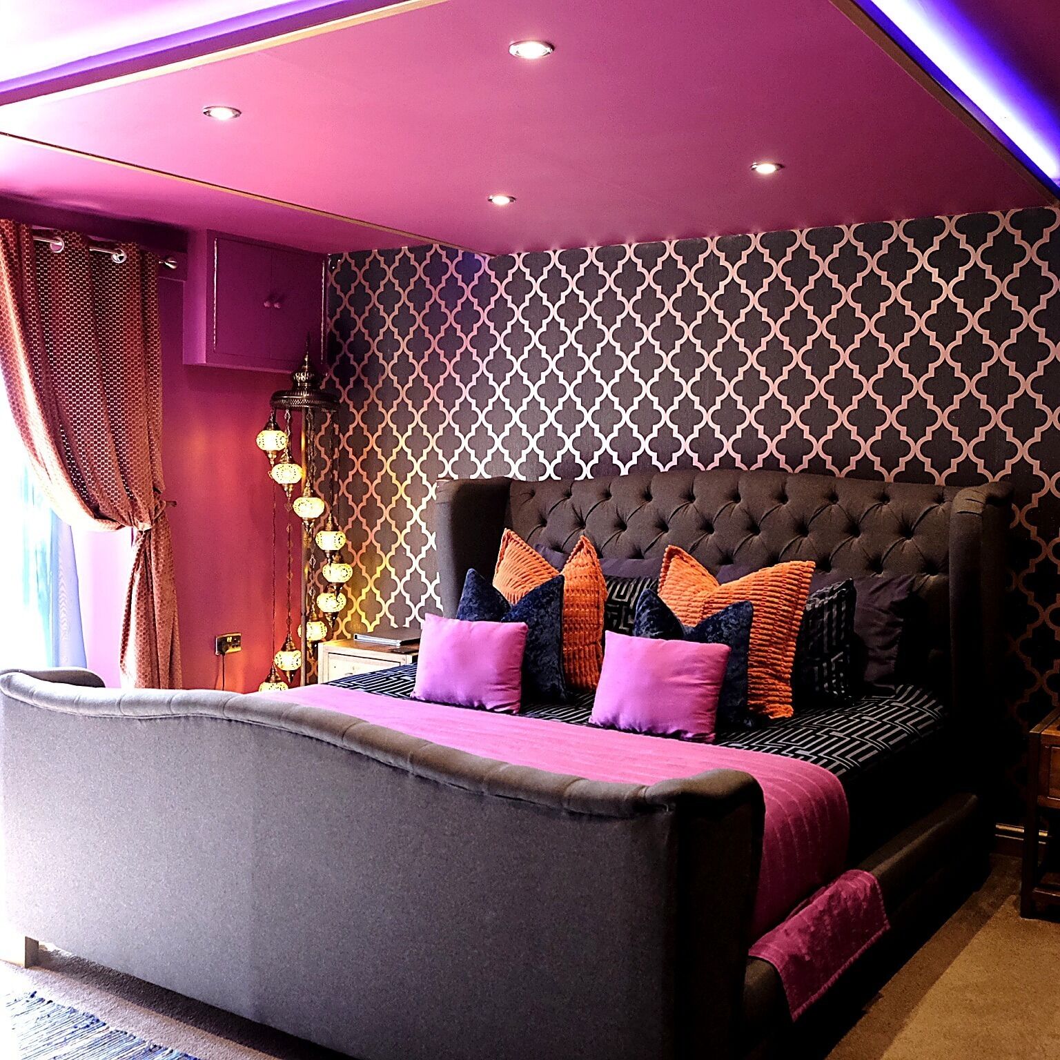 Un dormitorio con cabecera capitonada, pared con diseño y cama con muchas almohadas.