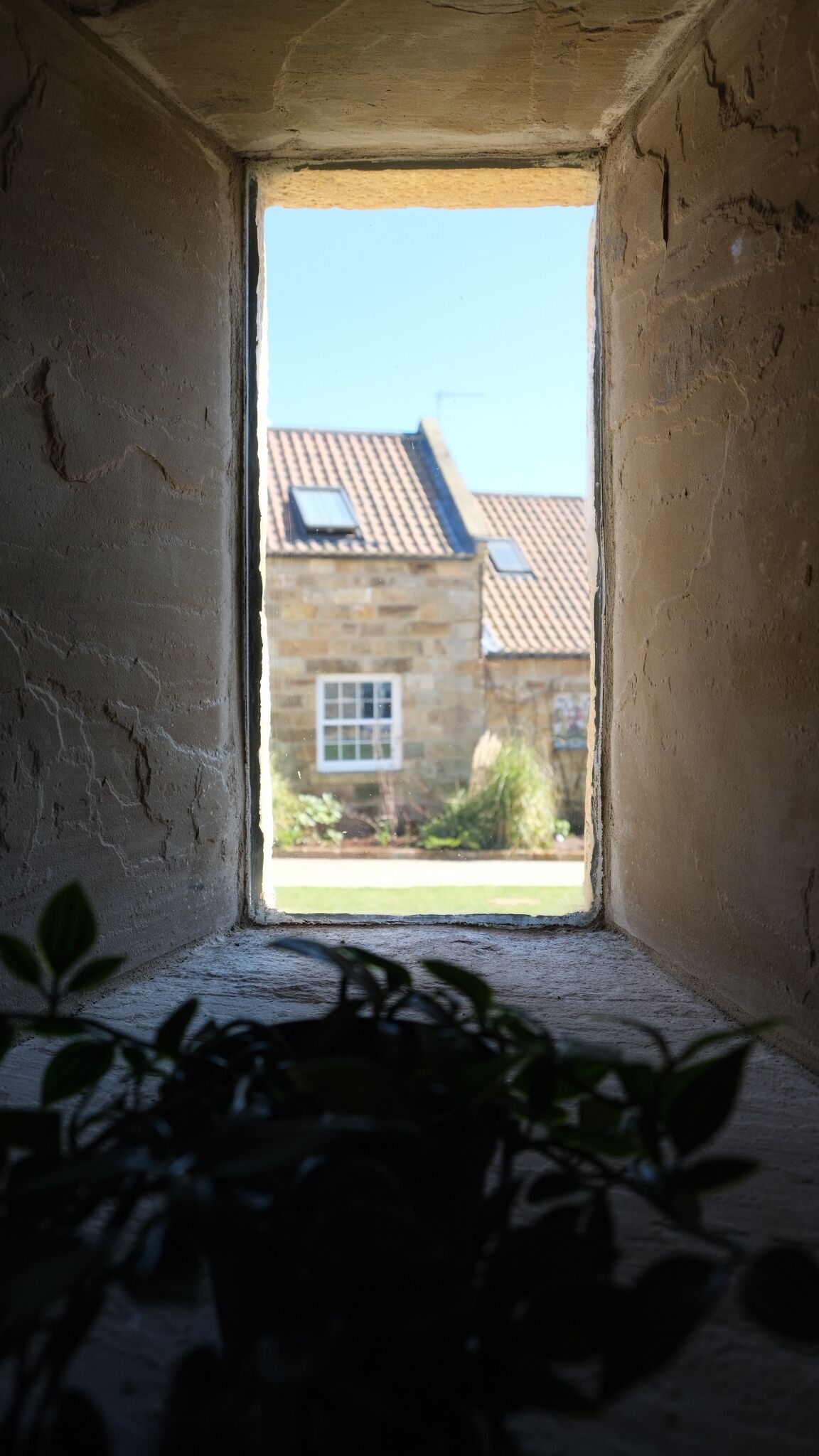A narrow window with a view of a stone building with a tiled roof.