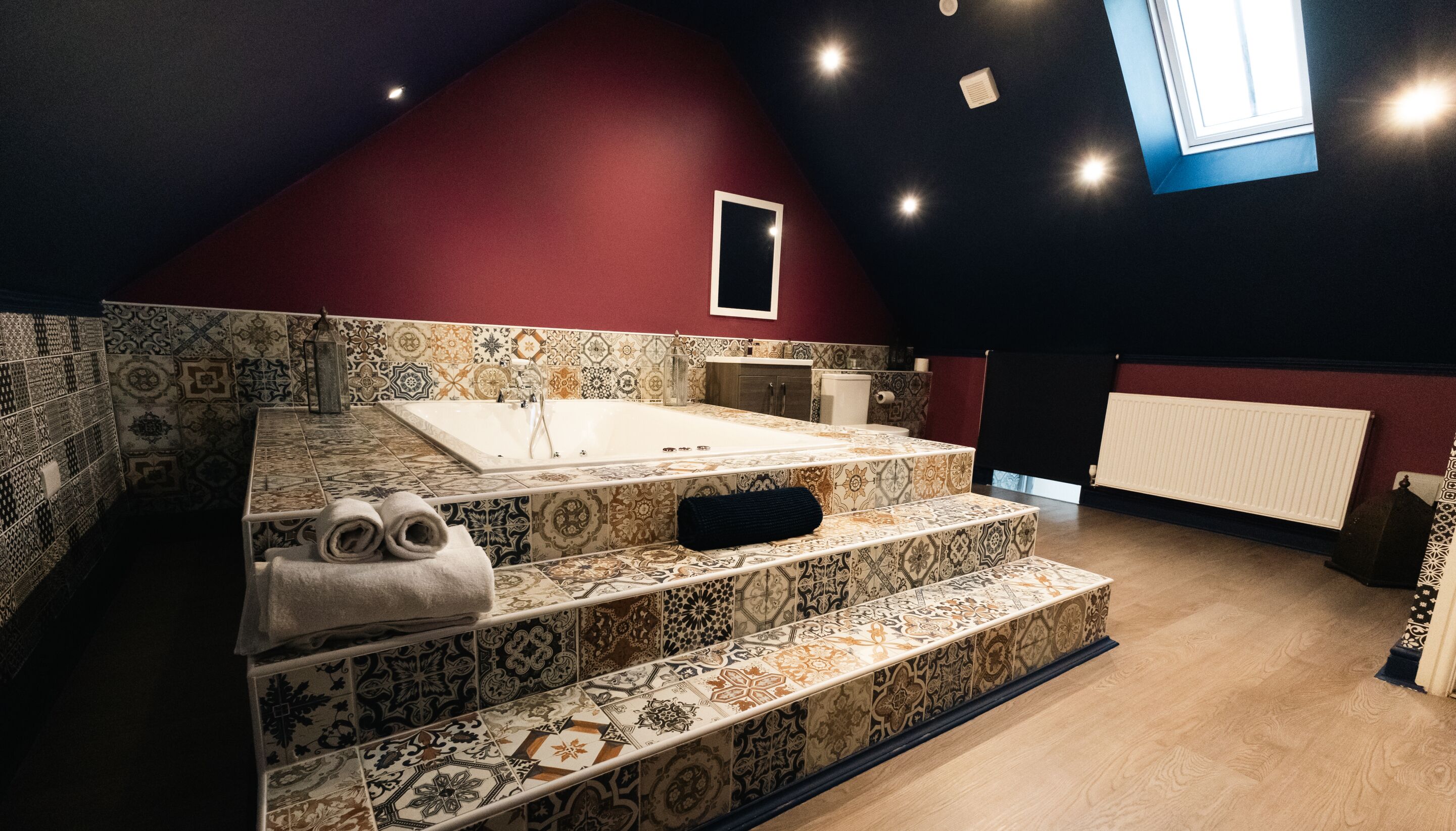 A bathroom with a freestanding bathtub, patterned tiles, and a red accent wall.