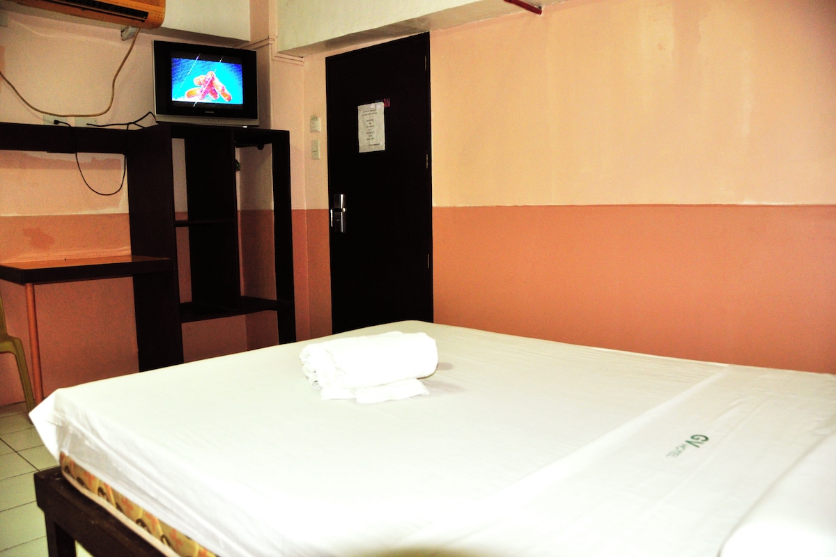 Una habitación de hotel con una cama, un televisor sobre un mueble y una puerta con un letrero.