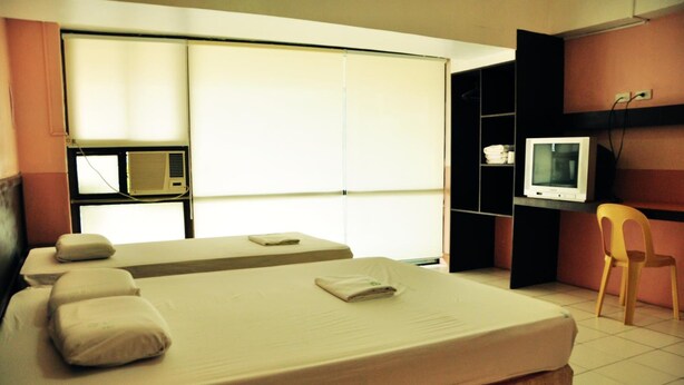 A hotel room with two beds, a television, a chair, and a window with blinds.