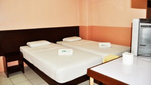 A hotel room with two single beds, each with a white mattress and a pillow, and a small bedside table with a lamp.