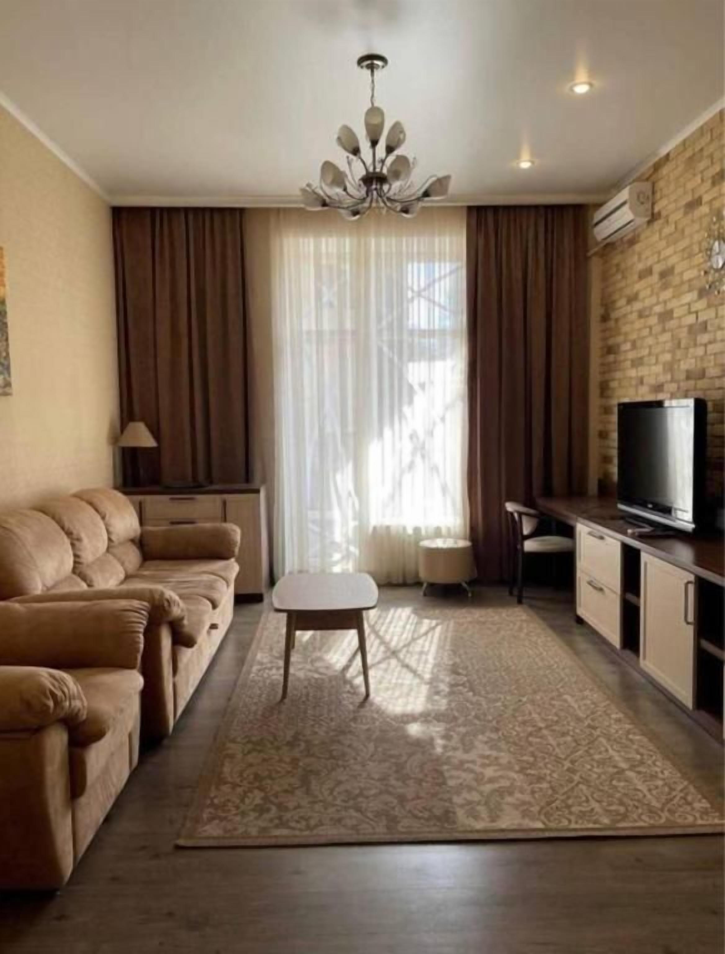 A living room with a sofa, a coffee table, a TV, and a brick wall.