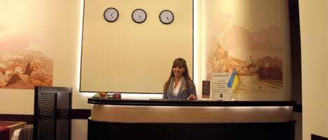 Una recepción con tres relojes encima, una mujer detrás del mostrador y una pared con un mural decorativo.
