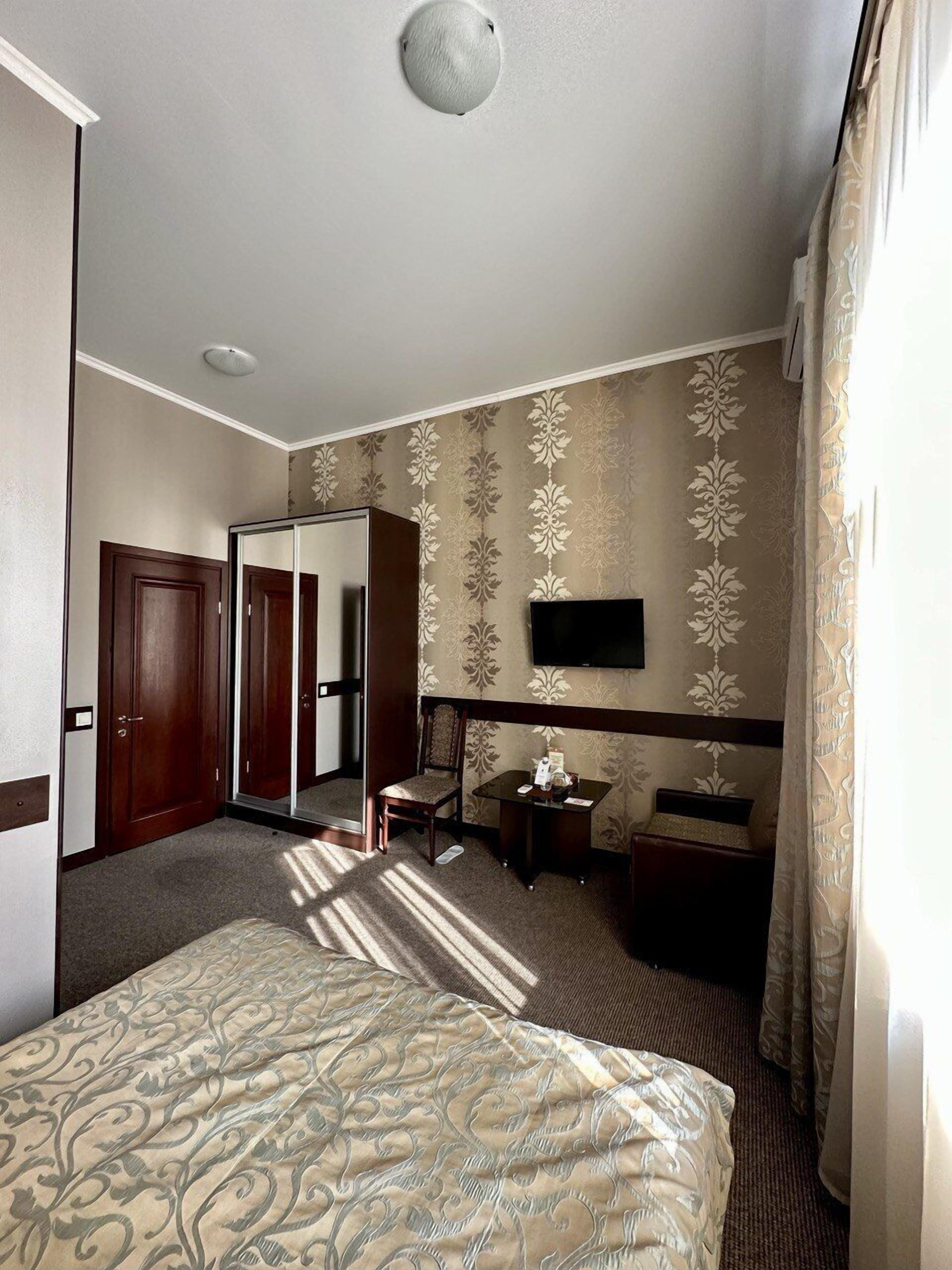 A hotel room with a bed, a desk, a chair, a TV, and a wardrobe.