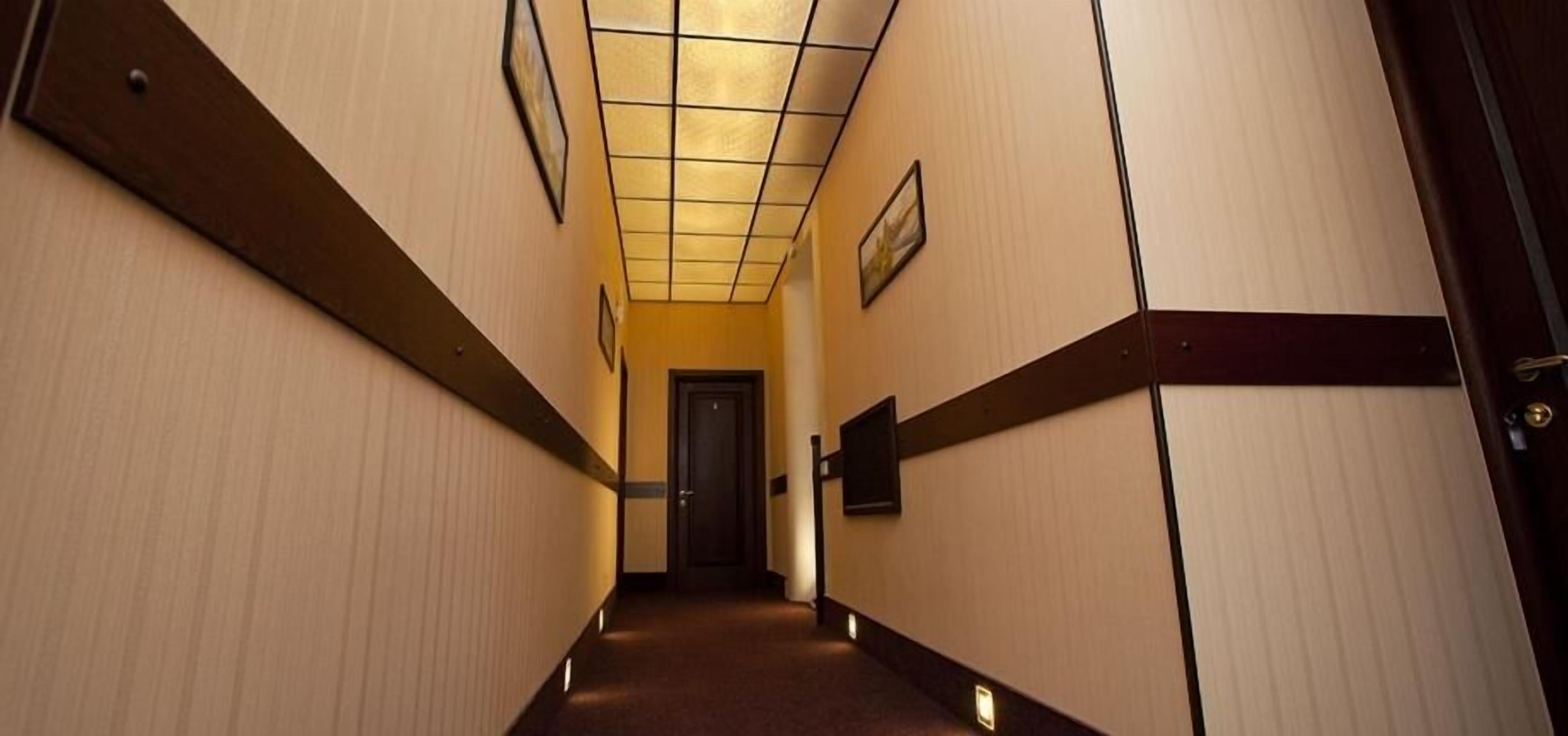 A hallway with a carpeted floor, wooden paneling, and a ceiling with a grid pattern.