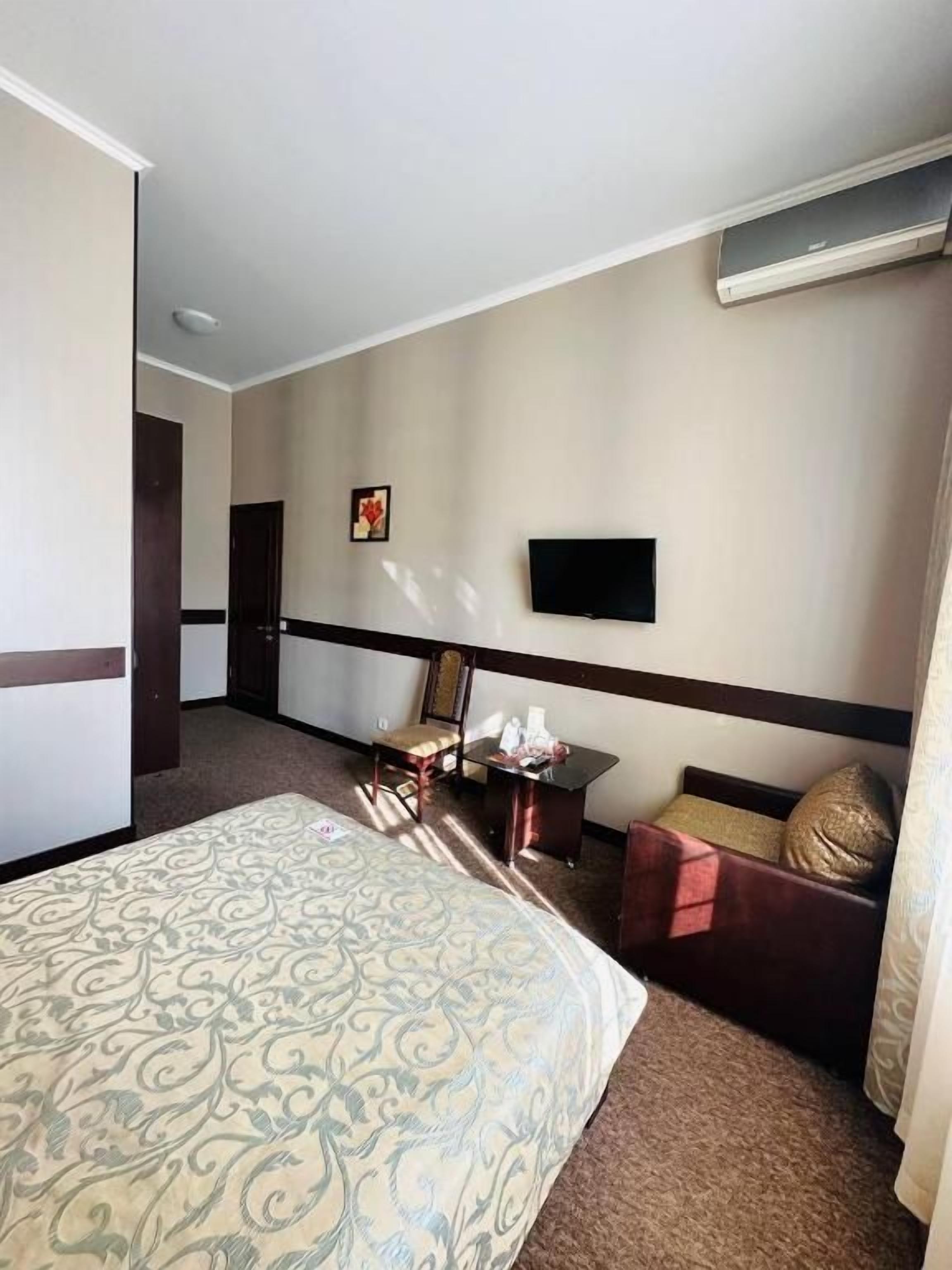 A hotel room with a bed, a desk, a chair, a flat-screen TV, and a window.