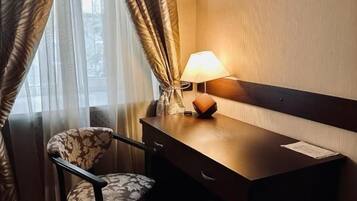 A hotel room with a desk, chair, lamp, and curtains.