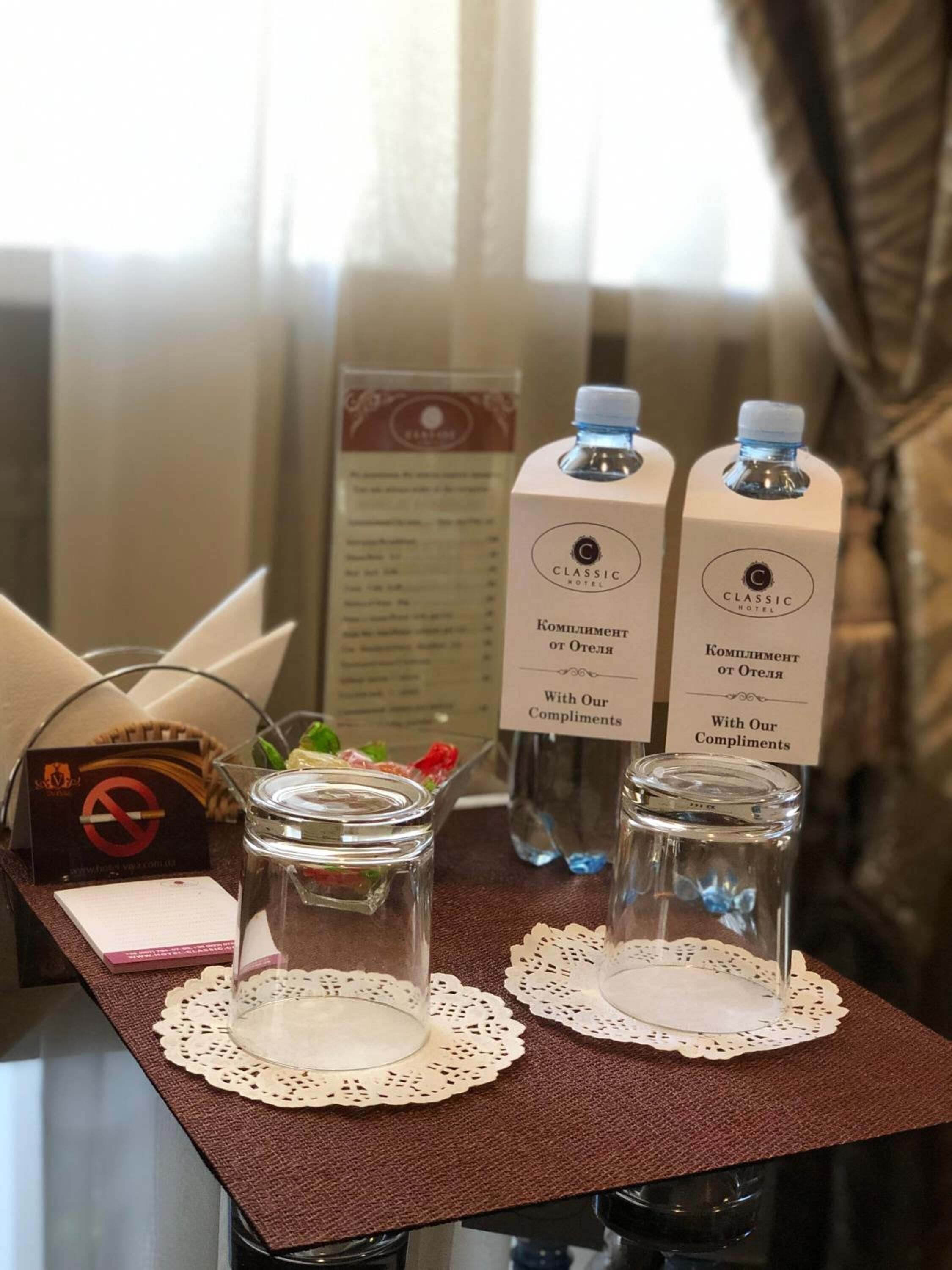 Ein Tisch im Hotelzimmer mit zwei Wasserflaschen, einem Glasbehälter, einer Speisekarte und einem Rauchverbot-Schild.
