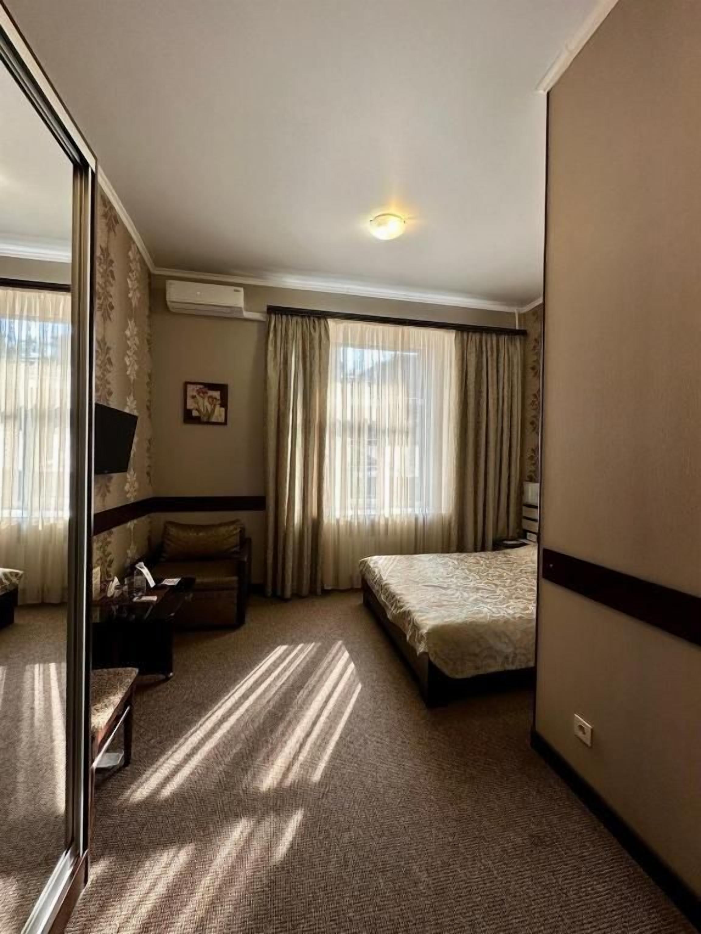 Una camera d'albergo con un letto, un divano, una scrivania e un'ampia finestra con tende.