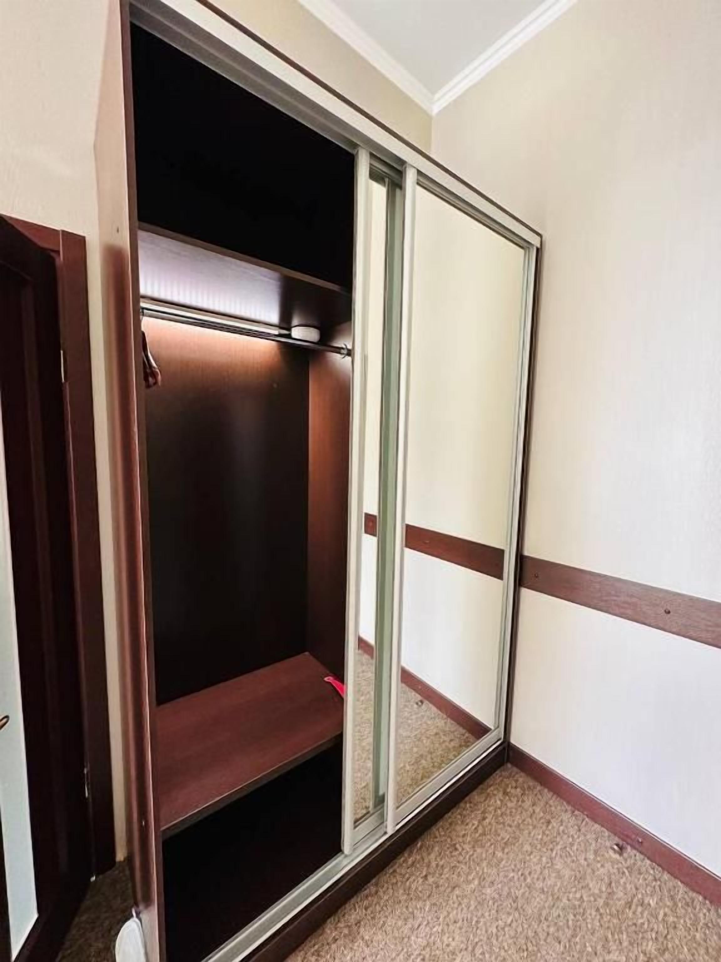 Een hoek van een kamer met een schuifdeurkast, vloerbedekking en een wand met horizontale plint.