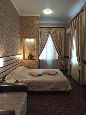 A hotel room with a large bed, a bedside table, a mirror, and a window with curtains.