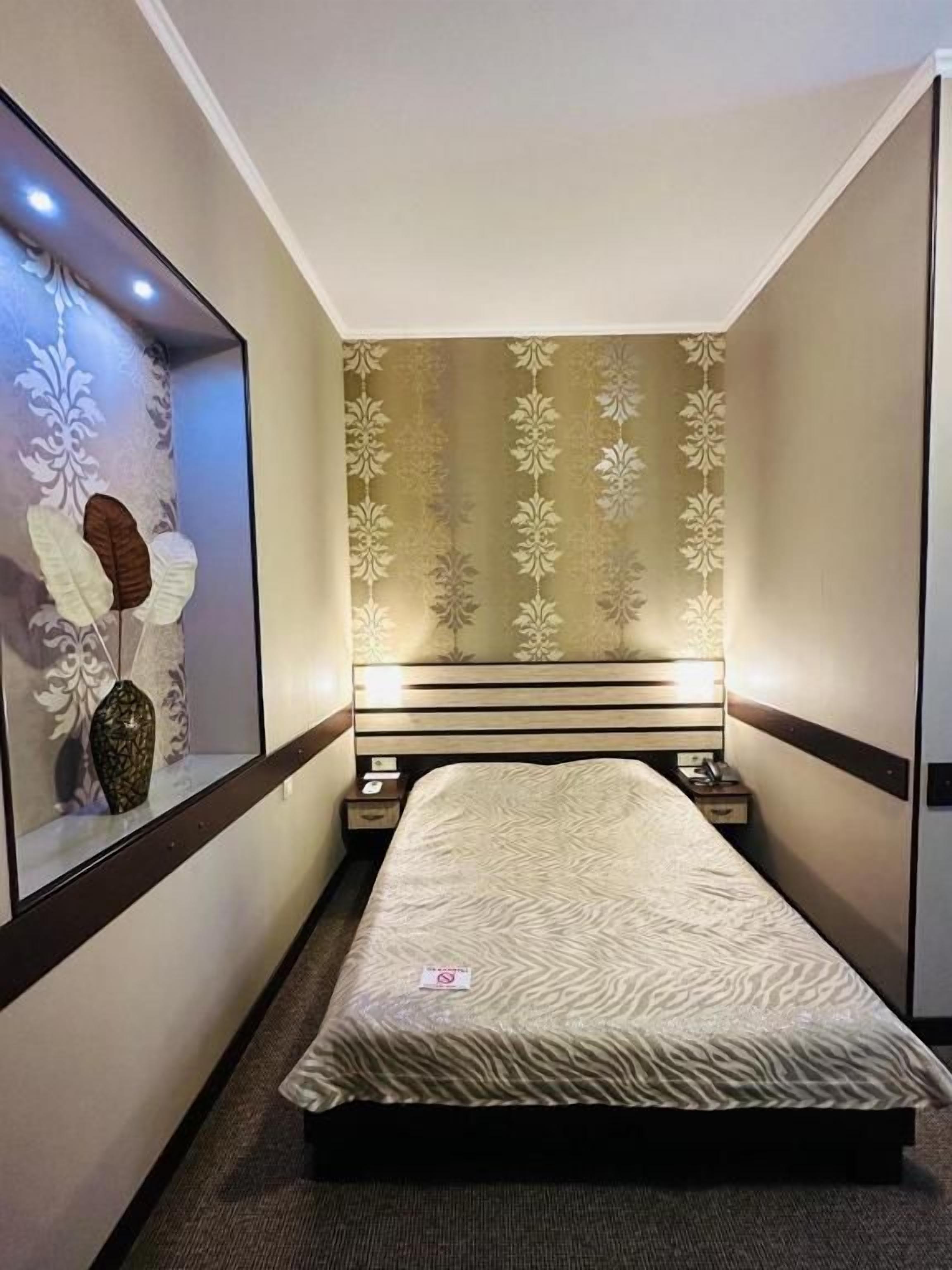 Een hotelkamer met een bed, een nachtkastje, een wandlamp en een decoratieve spiegel.