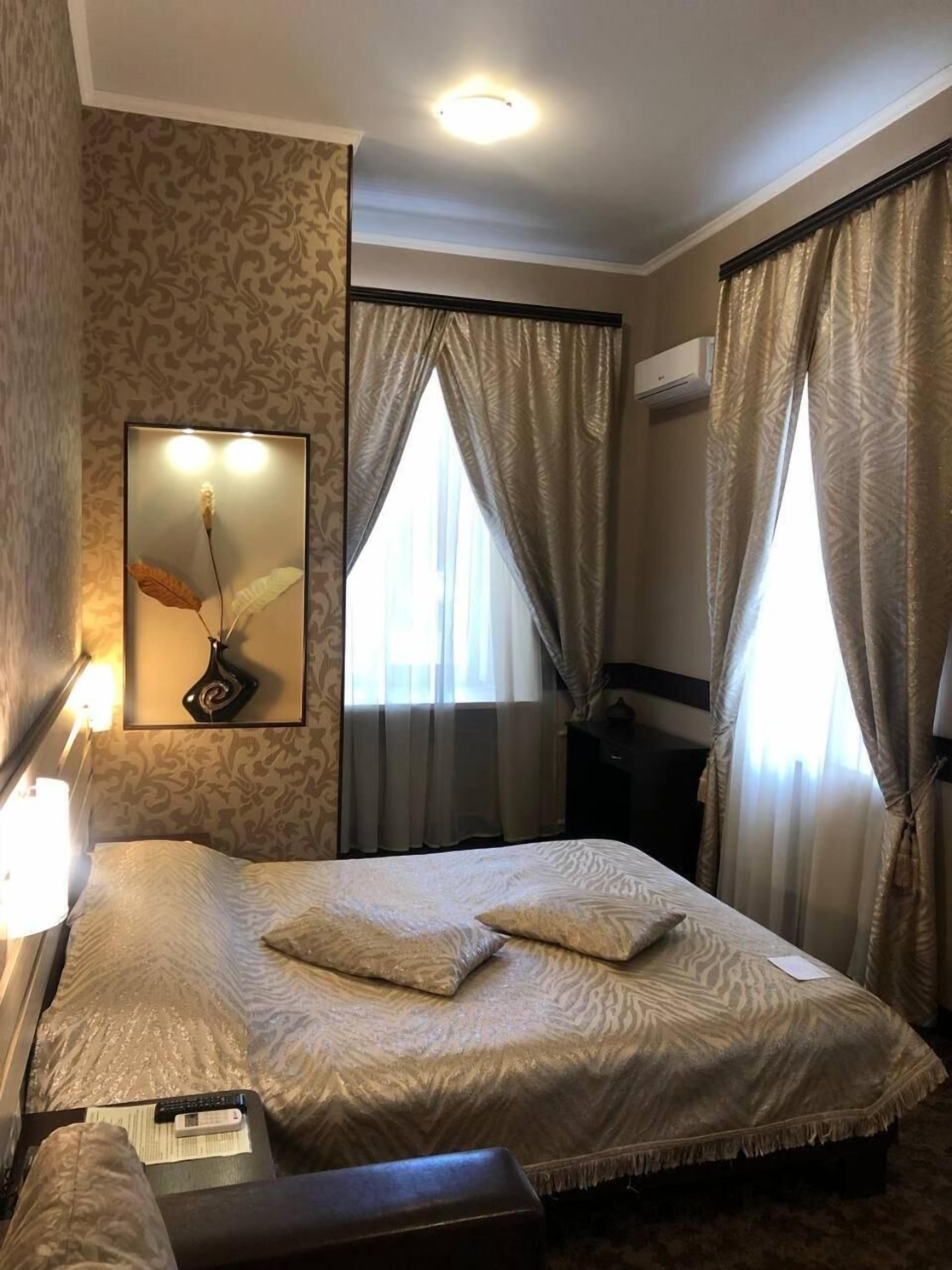 A hotel room with a bed, a bedside table, a lamp, a mirror, and curtains.