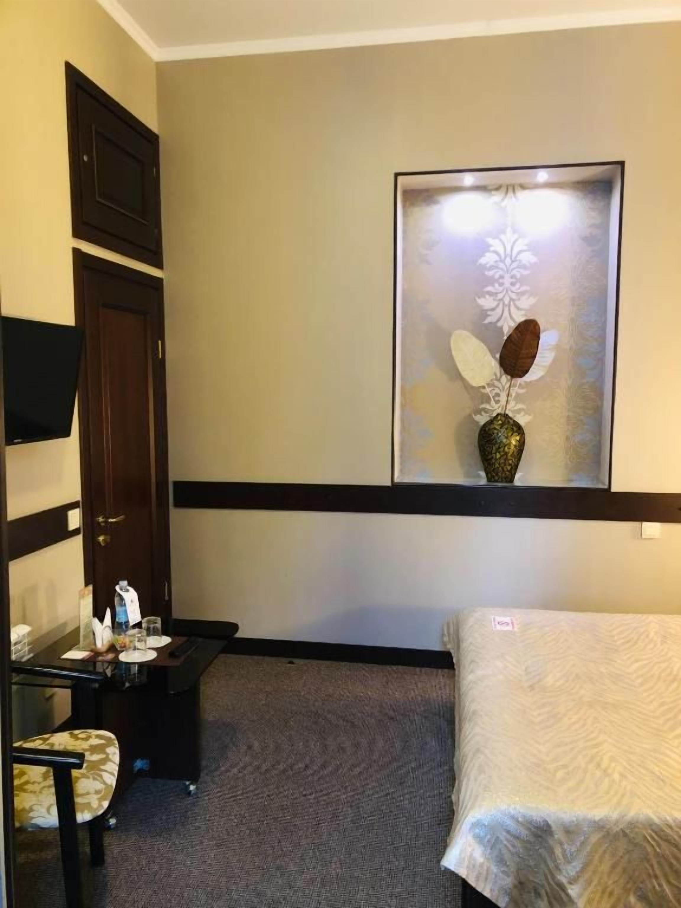 Habitación de hotel con cama, escritorio con silla, una mesita con un florero y un televisor montado en la pared.