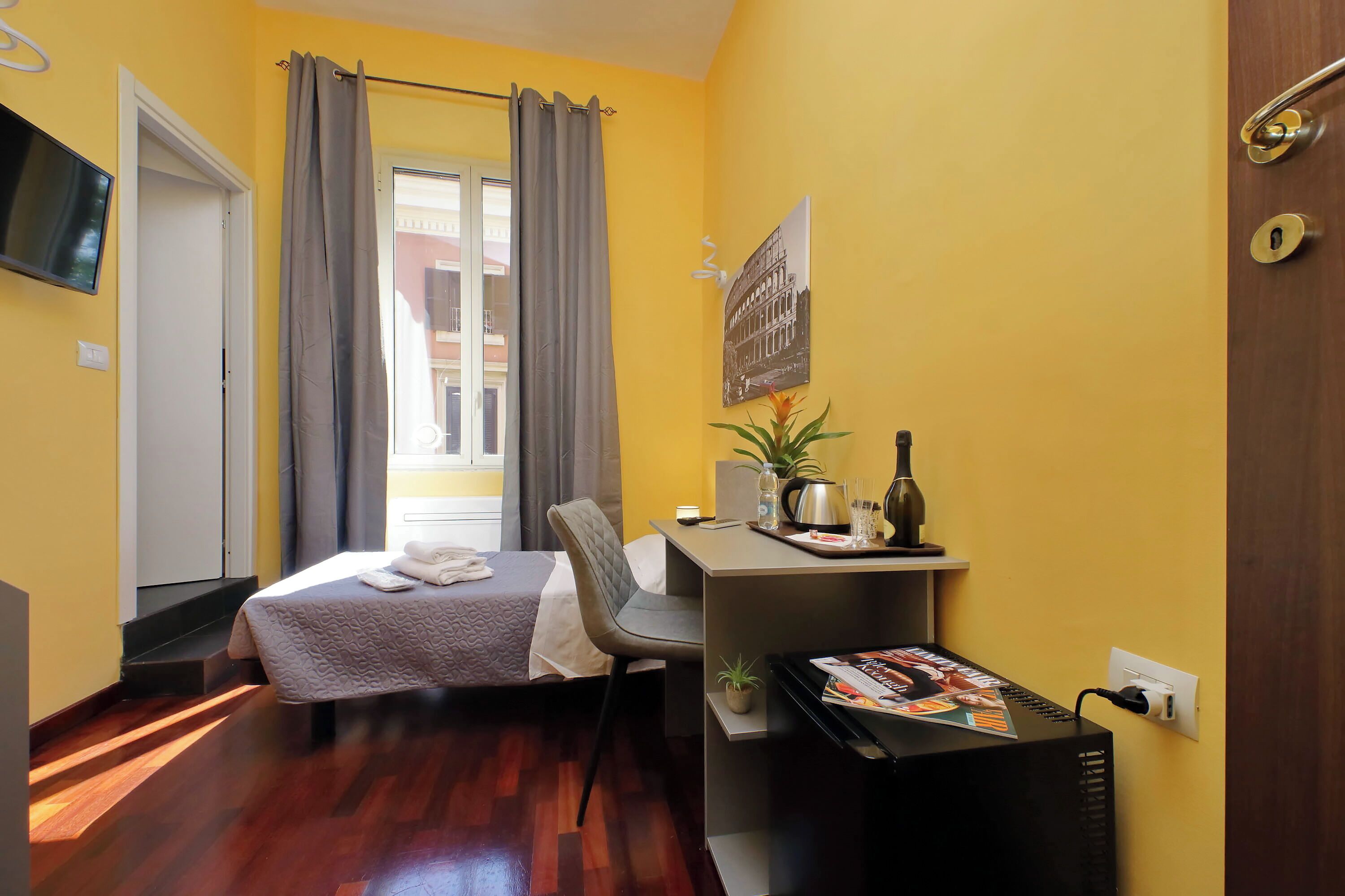 A compact hotel room with a bed, a desk, a chair, a TV, and a window with curtains.
