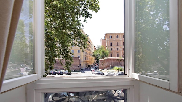 A view from a window with ornate ironwork, overlooking a street with parked cars and buildings. - New Moon (Rome)