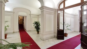 A grand hallway with a red carpet, white walls, and large windows. - New Moon (Rome)