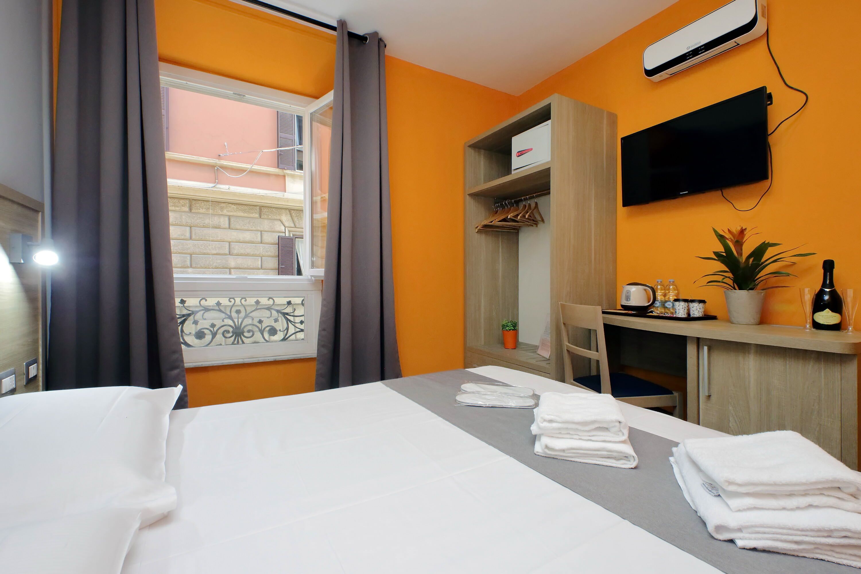Una habitación de hotel con cama, escritorio, televisión y ventana con cortinas.