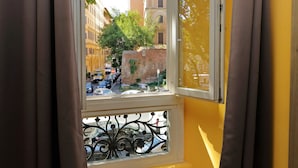 A window with a view of a street, a building, and a tree. - New Moon (Rome)