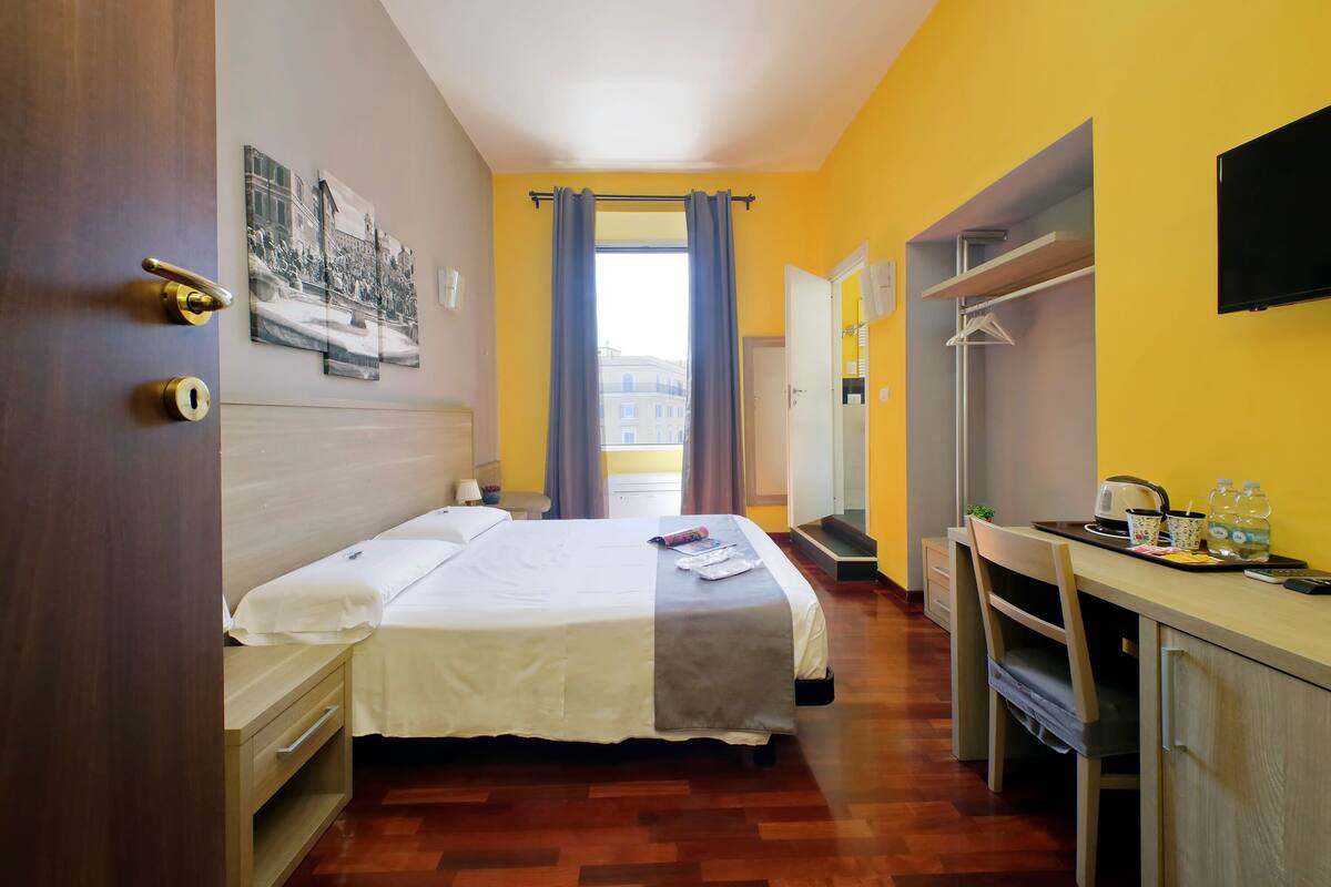 A hotel room with a bed, a desk, a chair, a TV, and a window with curtains.