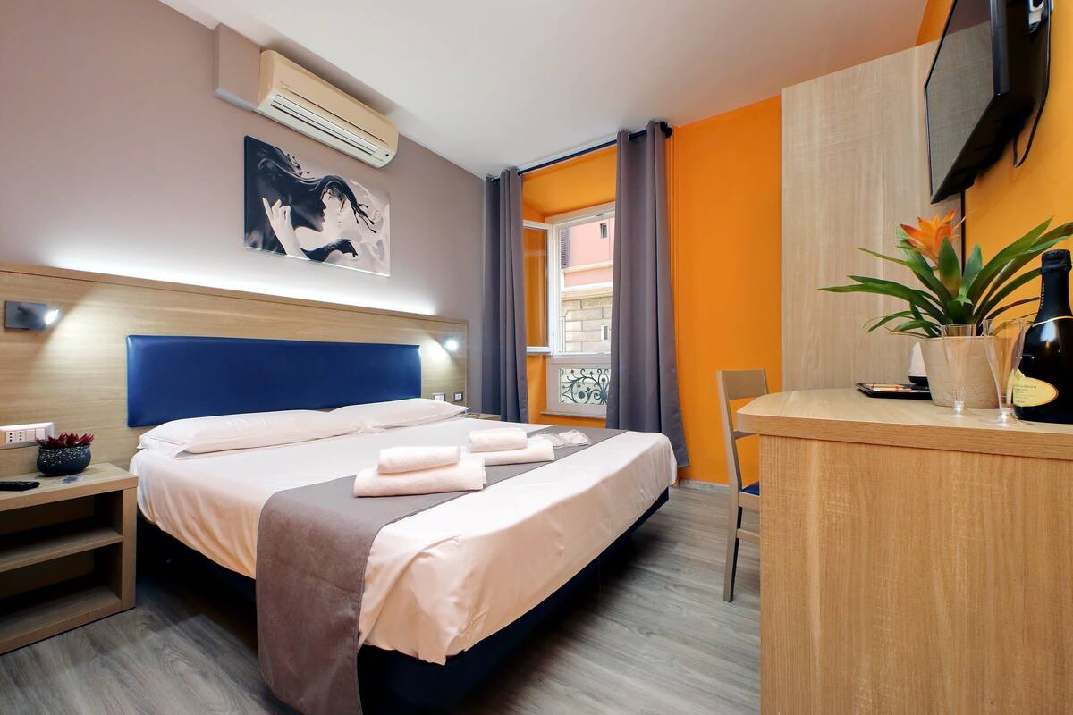 A hotel room with a bed, bedside table, and a desk with a chair.