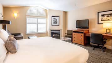 Habitación de hotel con una cama grande, un escritorio con computadora, un televisor, una chimenea y una ventana con persianas.