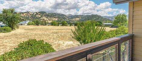 A residential property with a wooden deck, a fenced yard, and a view of a hilly landscape in the background.