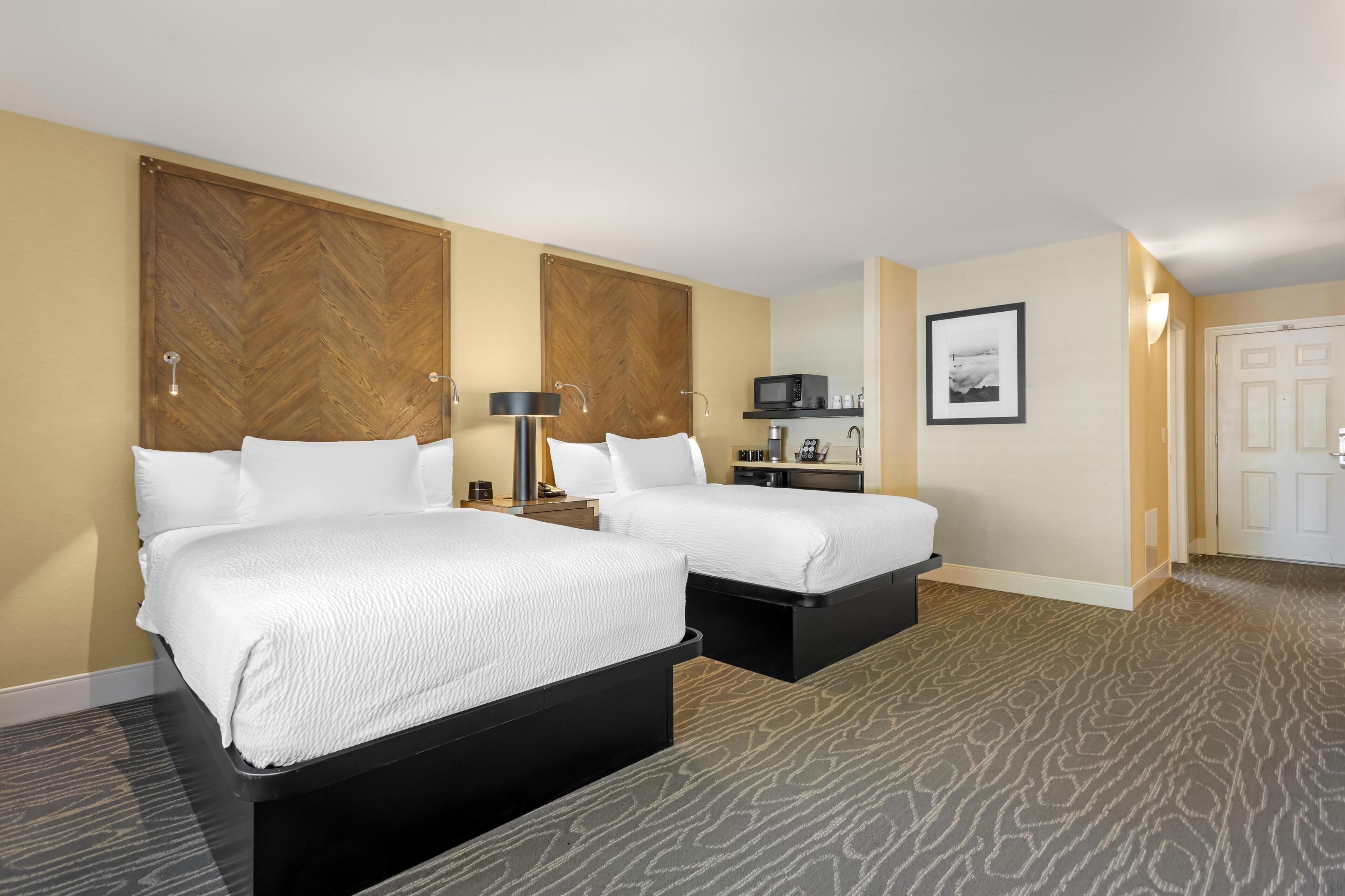 Ein Hotelzimmer mit zwei Betten, einer Mikrowelle, einer Kaffeemaschine und einem gerahmten Bild an der Wand.