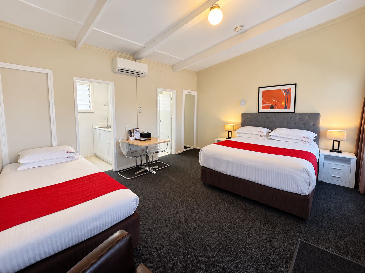 Une chambre d’hôtel avec deux lits, un bureau, une chaise, une table de chevet et un appareil de climatisation.