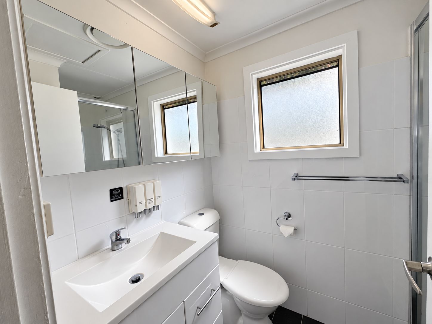 Une salle de bain moderne avec un lavabo blanc, des toilettes, un miroir et une fenêtre.