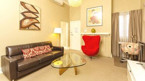 A living room with a brown leather sofa, a glass coffee table, a red chair, a chandelier, and a painting on the wall. - Club Motel (Wagga Wagga)