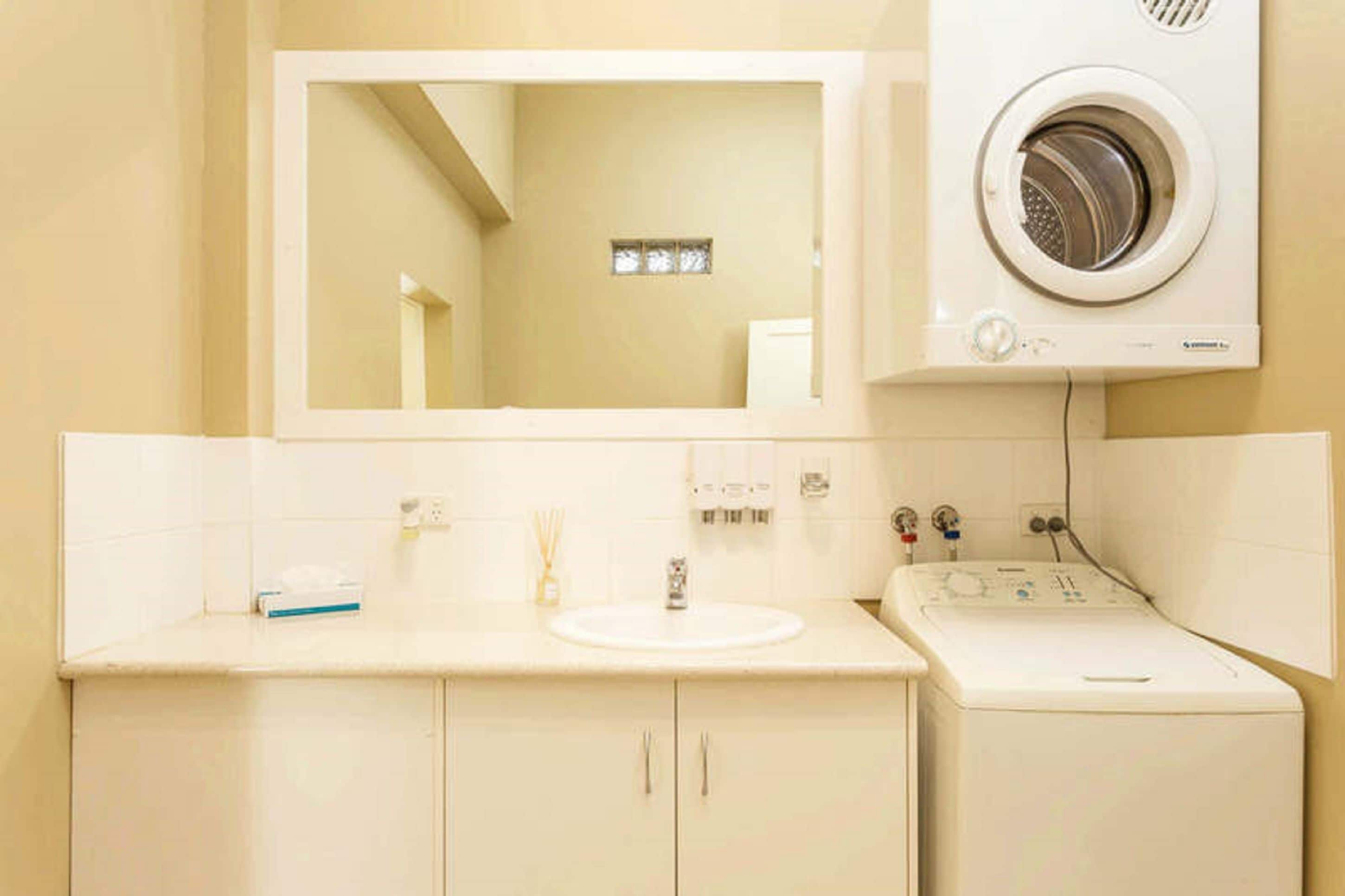 A bathroom with a sink, mirror, and a front-loading washing machine.