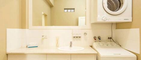 A bathroom with a sink, mirror, and a front-loading washing machine.
