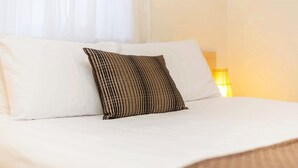 A neatly made bed with white linens and a striped pillow. - Club Motel (Wagga Wagga)