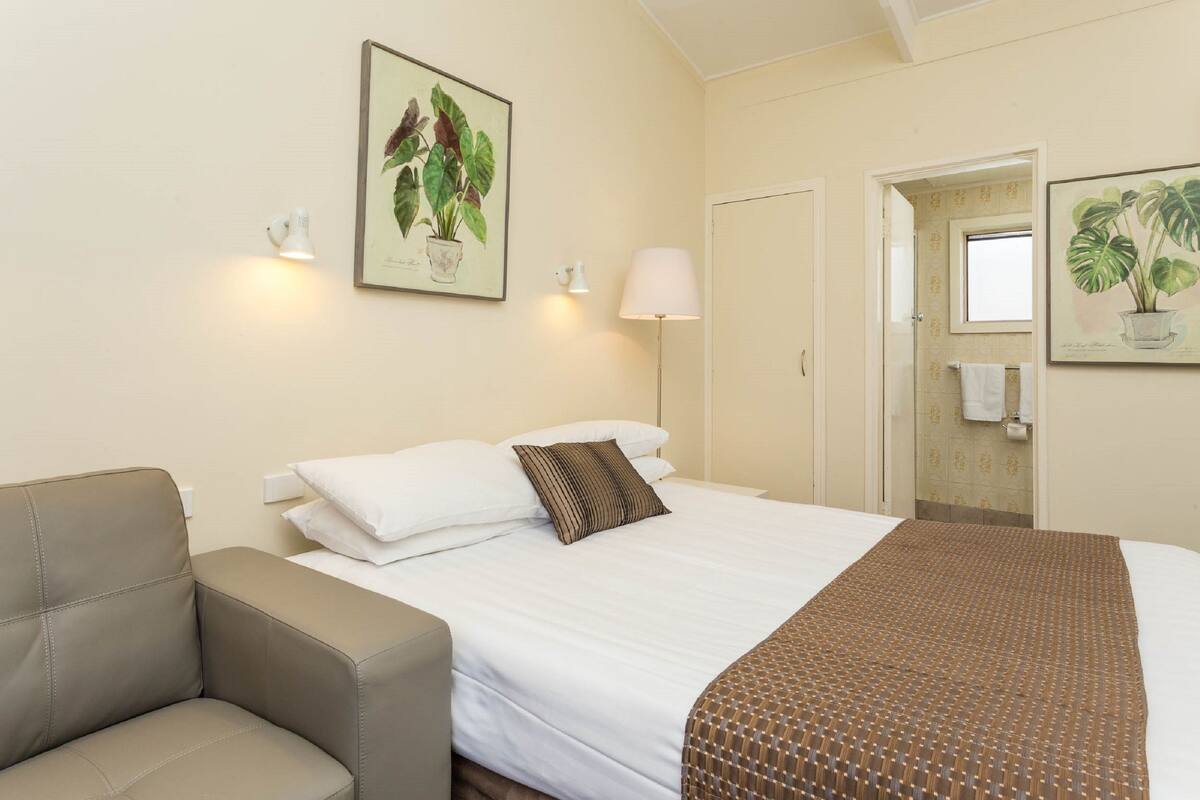A hotel room with a bed, a chair, a lamp, and two wall-mounted light fixtures.