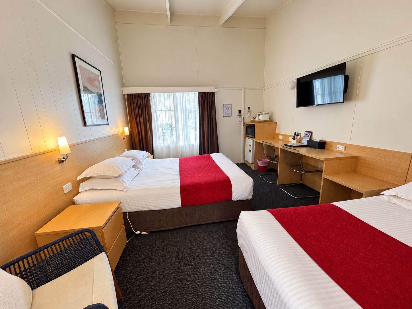 A hotel room with two beds, a desk, a television, and a window with curtains.