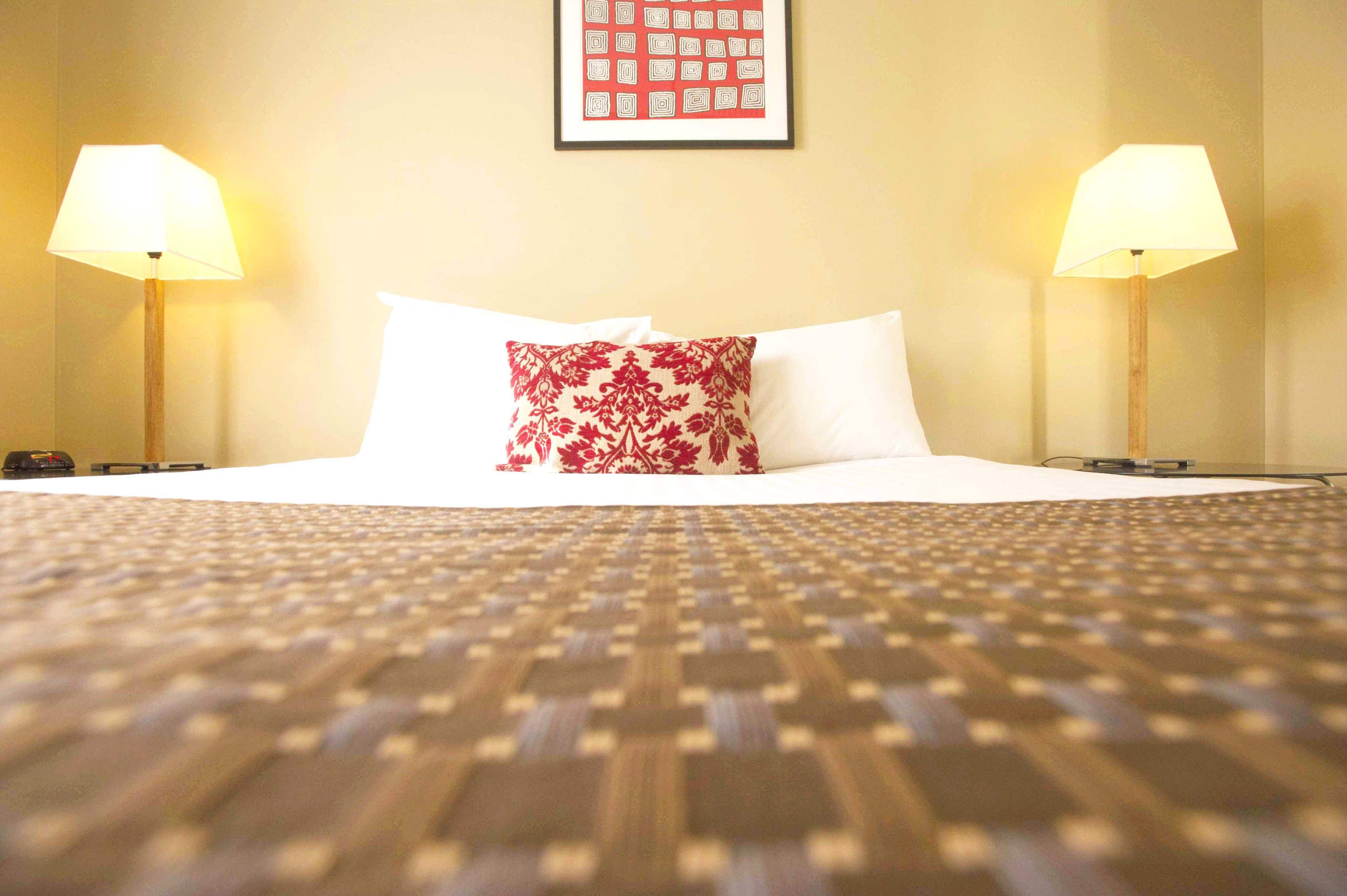 A hotel room with a neatly made bed, two bedside lamps, and a framed picture on the wall.
