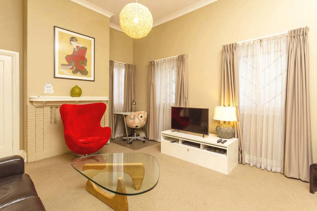 A living room with a glass coffee table, a red chair, a television, and a lamp.