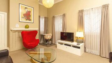 A living room with a glass coffee table, a red chair, a television, and a lamp.
