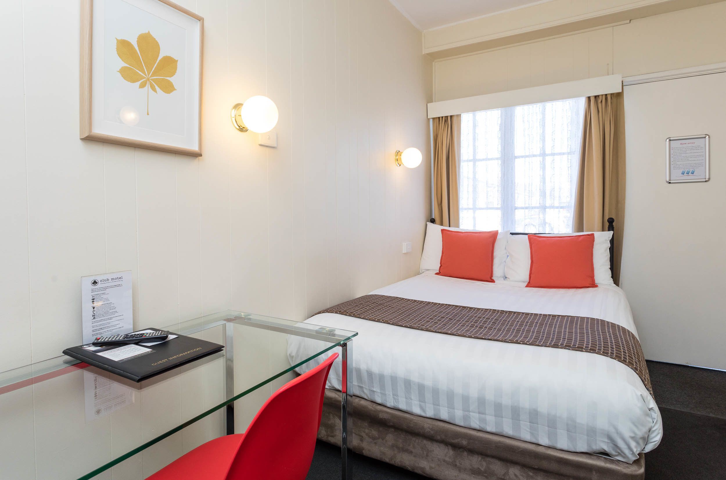 A hotel room with a bed, a desk with a chair, a framed picture on the wall, and two wall-mounted lights.