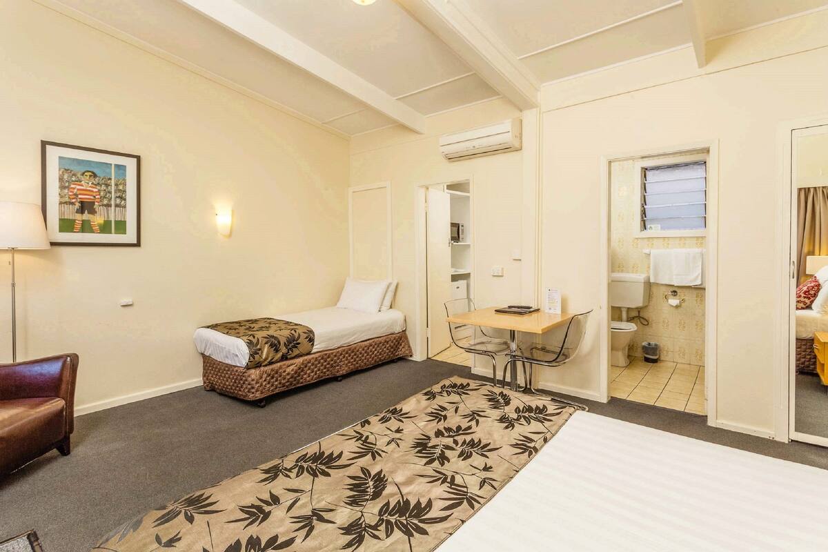 A hotel room with a bed, a small sofa, a desk with a chair, a bathroom, and a framed picture on the wall.