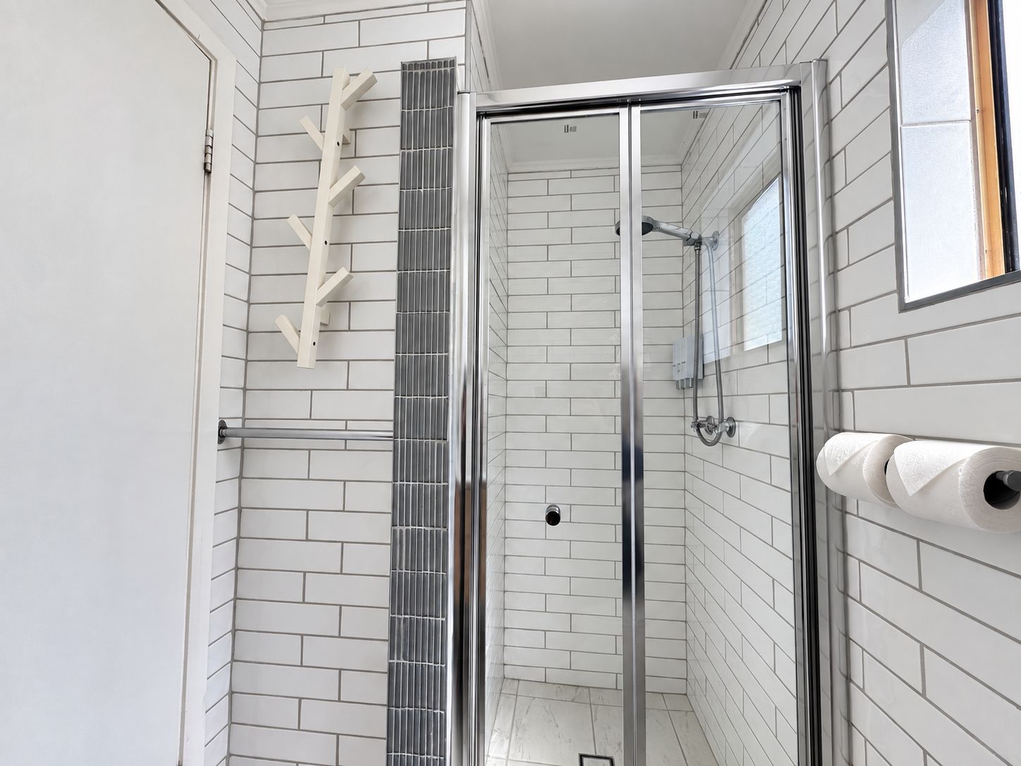 Un baño moderno con paredes de azulejos blancos, cabina de ducha de vidrio y toallero con toallas de papel.