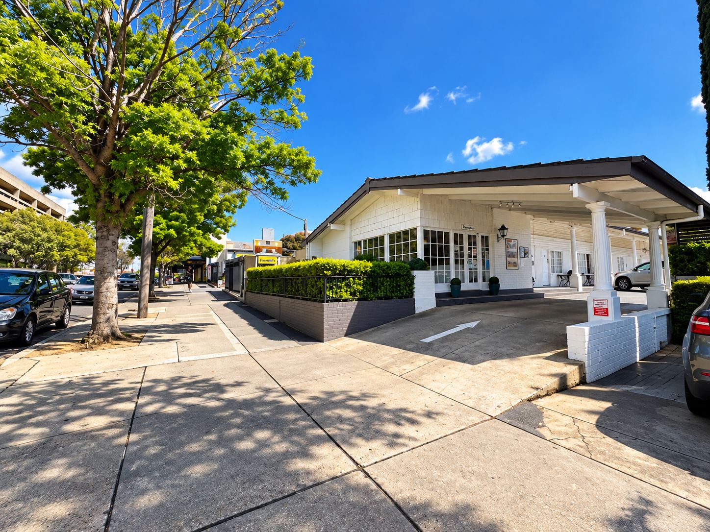 A gas station with a white building, a paved parking area, and a tree on the sidewalk.