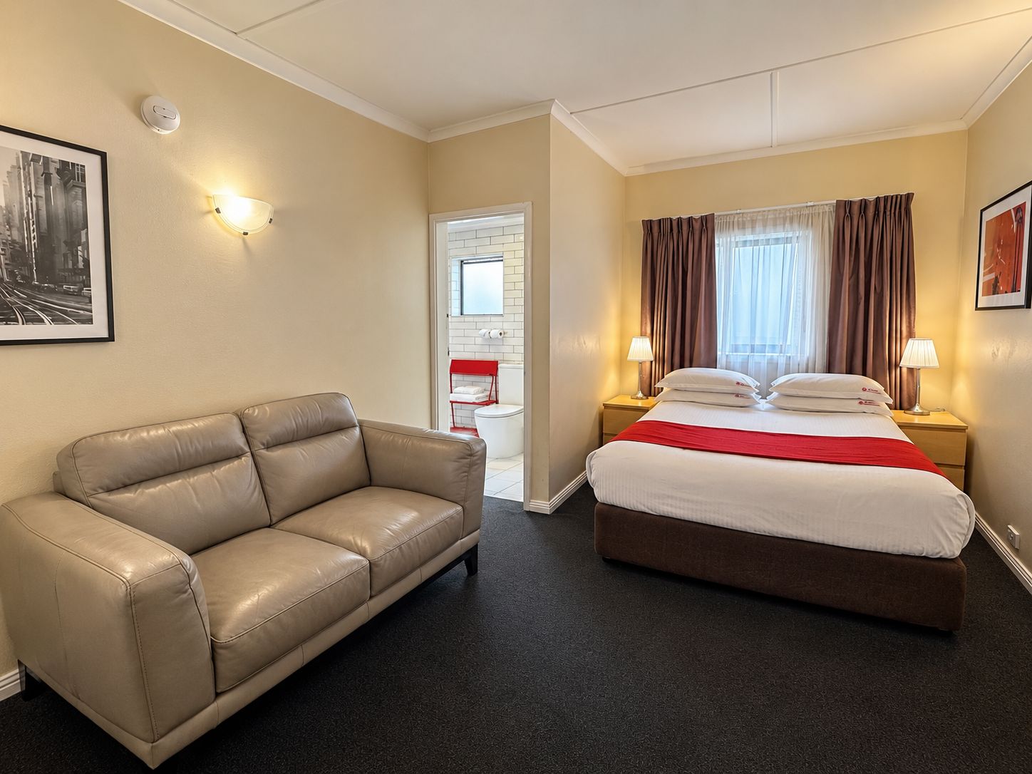 Quarto de hotel com cama, sofá de couro, mesa de cabeceira com luminárias e um quadro na parede.