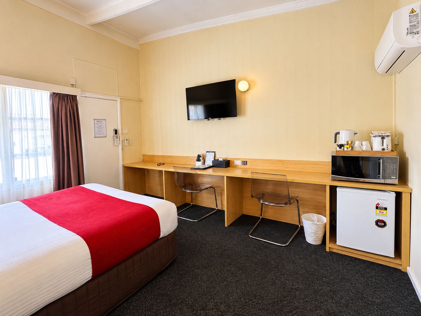 A hotel room with a bed, a desk, a TV, a microwave, and a mini-fridge.