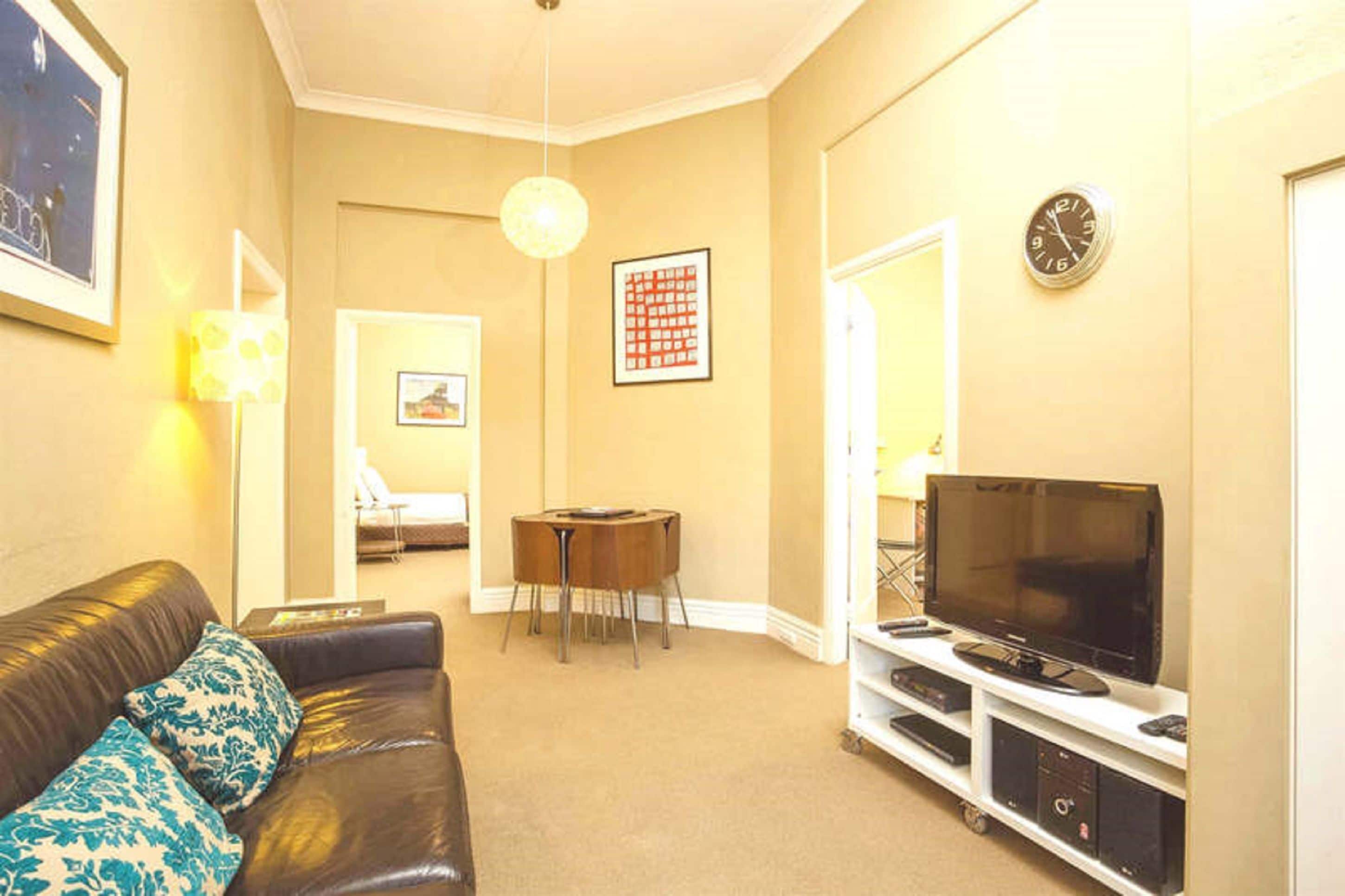 A living room with a leather sofa, a TV on a stand, a small table, and a framed picture on the wall.