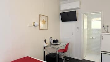 A compact room with a glass desk, a red chair, a framed picture, a black TV, and a white air conditioning unit.