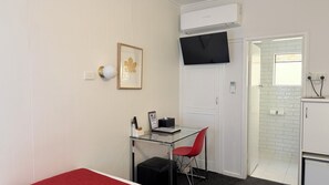 A compact room with a glass desk, a red chair, a framed picture, a black TV, and a white air conditioning unit. - Club Motel (Wagga Wagga)
